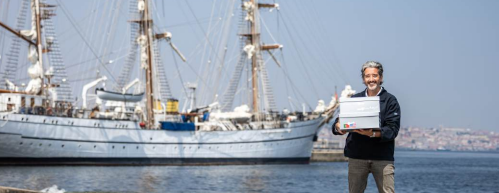 Ricardo Diniz holding letter boxes on the dock with the tall ship Sagres in the background.